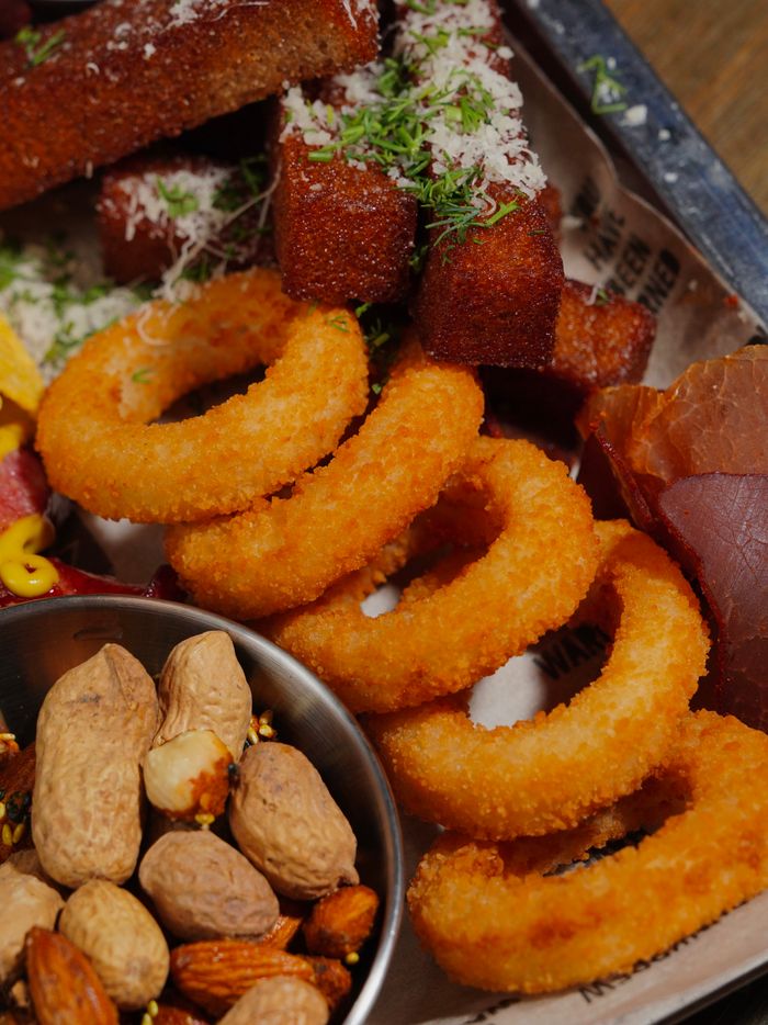 Delicious assortment of fried snacks including onion rings, breaded bites, and nuts on a tray.