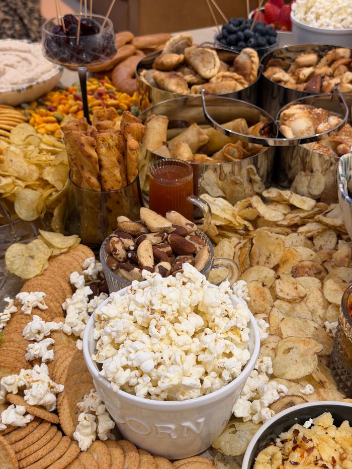 A variety of snacks and treats displayed on a buffet table with popcorn, chips, and mixed nuts.