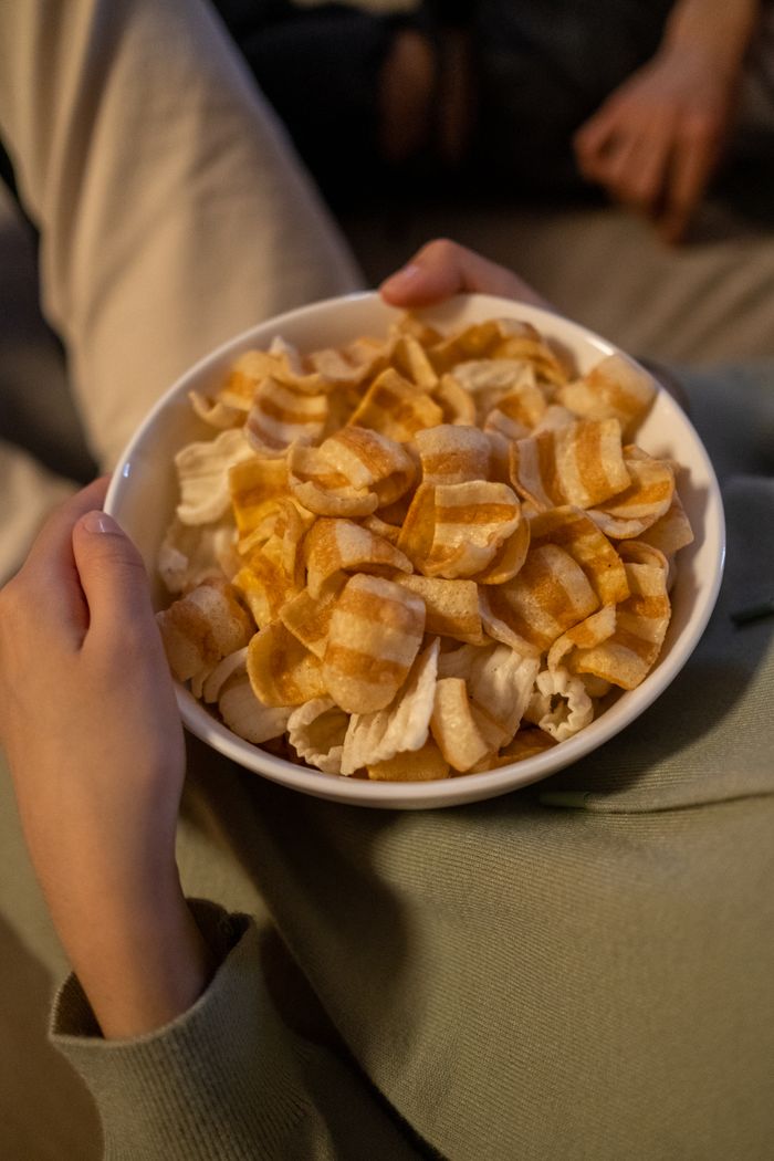 Person holding a bowl of striped puffs, perfect for a relaxing movie night at home.